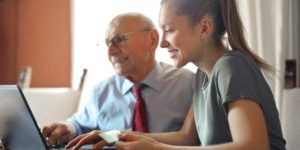 young woman helping senior man with payment on internet using laptop